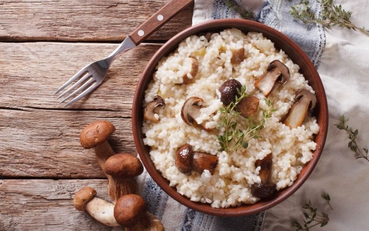 Risotto with mushrooms in a bowl with fork and napkin beside the bowl on the table - The Proud Italian