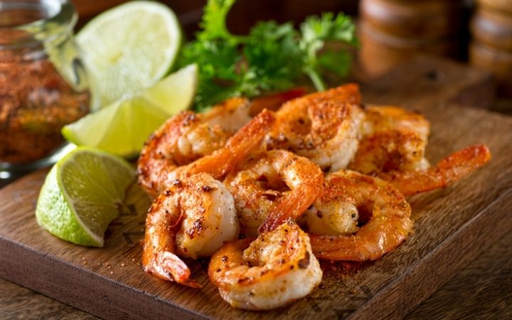Shrimps on chopping board with slices of lime beside - The Proud Italian