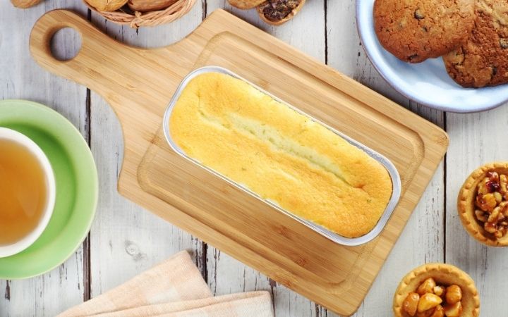 Italian Lemon Pound Cake in baking cast on cutting board with ingredients in bowls around the cake - The Proud Italian