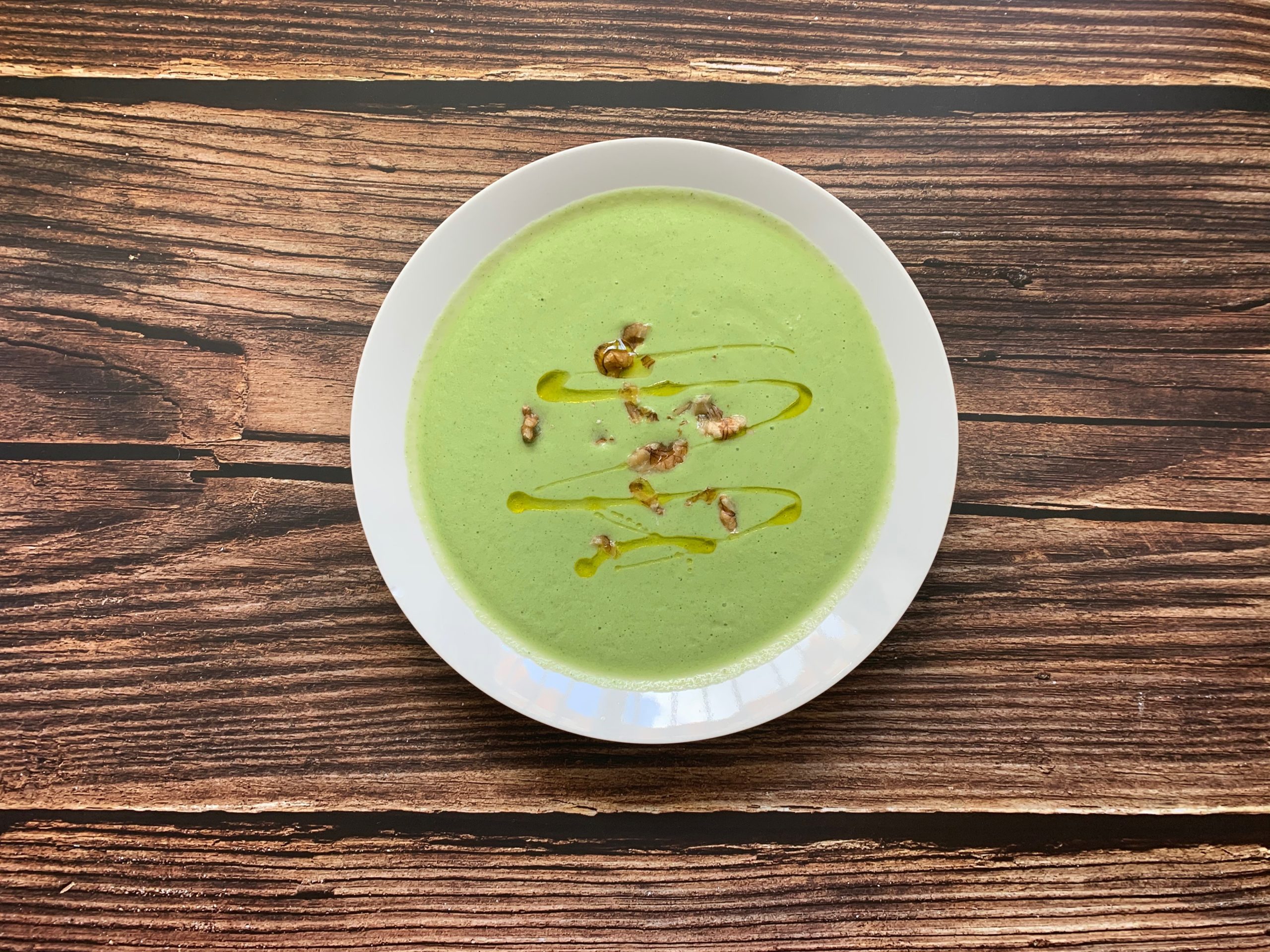 a white bowl of green sausage and broccoli soup on a wooden table