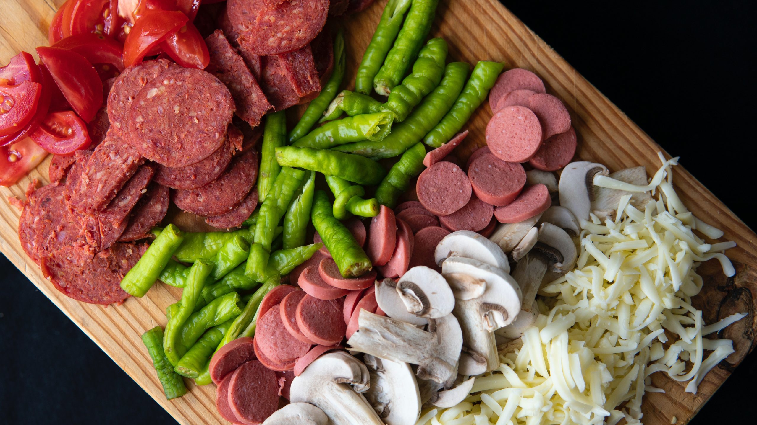  tomatoes, peppers, Italian sausages, mushrooms and grated cheese on a wooden board